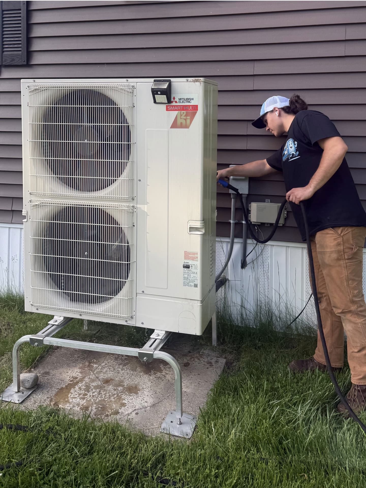 Technician rinsing an outdoor unit with a controlled, low-pressure spray