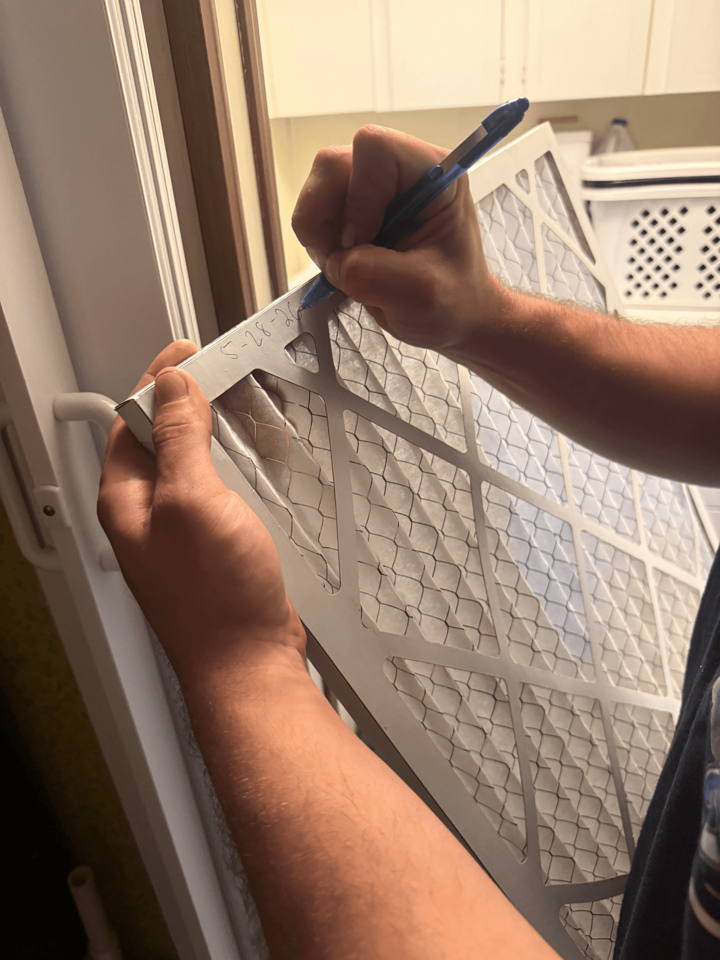 Tech writing the install date on a fresh filter — we track every visit